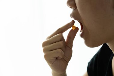 Genç ve güzel Asyalı bir kadın elinde balık yağı kapsülü tutuyor. Beslenme ve vitamin takviyesi ürünü. Kadının elindeki yumuşak Gell hapı..