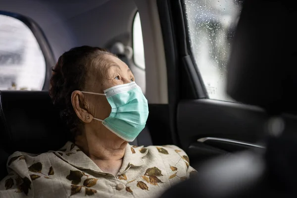 80-90 yaşları arasında çok yaşlı bir Asyalı kadın kişisel arabasıyla seyahat ediyor, yaşlı bir kadın seyahat sırasında koruyucu yüz maskesi kullanıyor. Coronavirus veya COVID-19 pandemik konsept. COVID19 salgını.