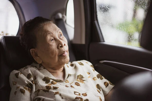 Cheerful Asian old woman taking a vehicle seat at the back, woman traveling by taxi during raining. Retirement in senior people portrait with copyspace.
