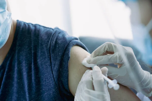 Doctor preparing a dose of vaccine for injection at patient left arm close up with copyspace. Healthcare and medical service concept. COVID-19 or coronavirus cure vaccine injection.