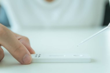 Hijyen koruyucu yüz maskesi takan Asyalı genç bir kadın SARS 2019-nCoV COVID-19 Coronavirus antijen hızlı test kiti kullanıyor. Evde tarımsal test kiti. COVID-19 antijen hızlı testi.