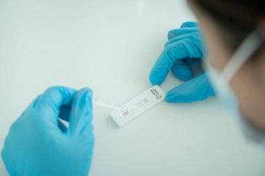 Hijyen koruyucu yüz maskesi takan Asyalı genç bir kadın SARS 2019-nCoV COVID-19 Coronavirus antijen hızlı test kiti kullanıyor. Evde tarımsal test kiti. COVID-19 antijen hızlı testi.