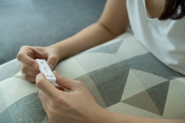 Hijyen koruyucu yüz maskesi takan Asyalı genç bir kadın SARS 2019-nCoV COVID-19 Coronavirus antijen hızlı test kiti kullanıyor. Evde tarımsal test kiti. COVID-19 antijen hızlı testi.