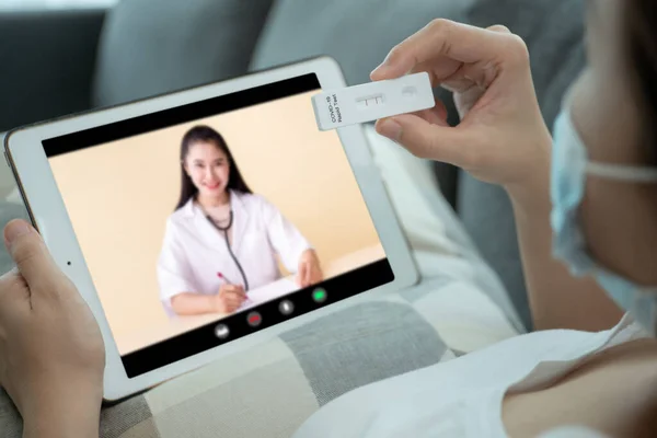 SARS 2019-nCoV COVID-19 Coronavirus antijen hızlı test kiti kullanan, hijyen koruyucu yüz maskesi takan Asyalı genç bir kadın - evde tarım test kiti ve video aracılığıyla doktorla test sonuçlarına danışmak.