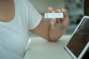 Boş ekran kırpma yolu ile izole edilmiş modern tablet. COVID-19 antijen testi sonucu pozitif çıktıktan sonra bir doktorla çevrimiçi video görüşmesi için tablet kullanan Asyalı genç kadın.