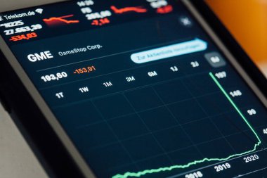 BERLIN, GERMANY - JANUARY 29, 2021: Close up to chart of GameStop stock hype amongst fight between small investors organized through Reddit and hege funds on the screen of an iPhone 7 Plus with personalized background.