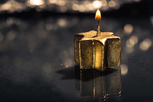 Lit golden candle with reflection and bokeh background