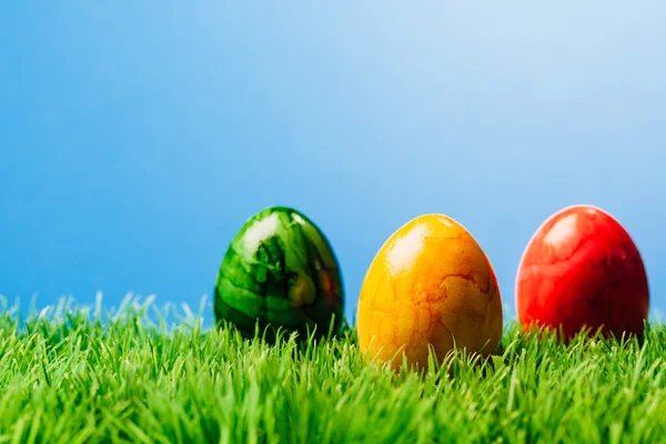 Tres huevos de Pascua en la hierba, fondo azul —  Fotos de Stock