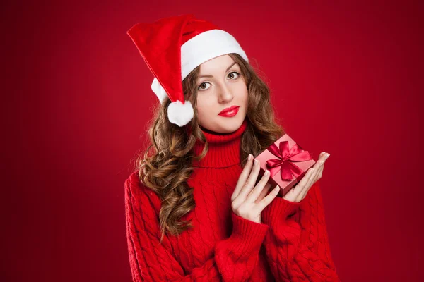 Girl in red sweater holding Christmas present wearing Santa Clau — Stock Photo, Image