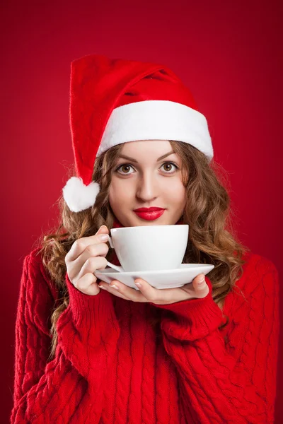 Krásná brunetka v klobouk Santa Clause drží bílý hrnek Stock Snímky