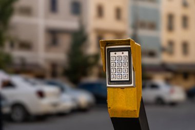 Elektronik tuş takımı açık hava park alanındaki sarı direğe monte edildi. Arka planda bulanık arabalarla güvenli erişim kontrol teknolojisi..