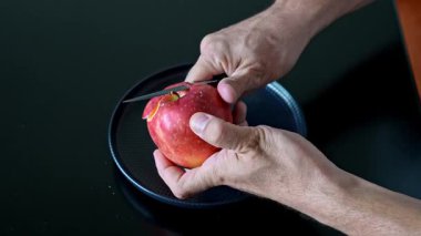 Kırmızı elmayı bıçakla soyan adam. Evdeki mutfakta dikkatli meyve hazırlama sürecinin yakın görüntüsü.