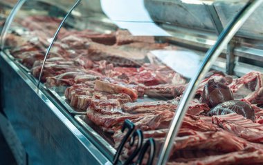 Bir kasapta çeşitli et kesimlerinin canlı bir gösterisi, cam altında çeşitli taze ürünler sergileniyor..