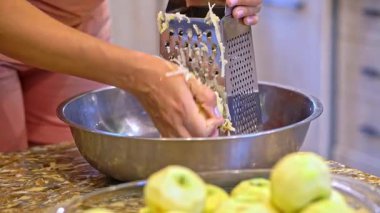 Closeup view of grating fresh apples on a hand grater. Simple food preparation process in a home kitchen environment.