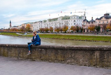 Avusturya 'nın Salzburg şehir merkezinde Salzach nehrinin setinde oturan bir kadın.