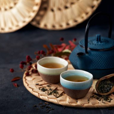 Koyu arkaplanda yaprakları olan yeşil çay fincanları ve çaydanlık. Seçici odaklanma. Japon çay töreni.