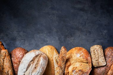Koyu yüzeyde farklı ekmek türleri olan bir arka plan. Kapatın. Metin için boş alan. Fırın kavramı.