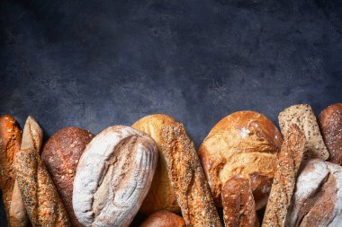 Koyu yüzeyde farklı ekmek türleri olan bir arka plan. Kapatın. Metin için boş alan. Fırın kavramı.