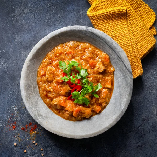 Indian food recipe. Chicken tikka masala spicy curry meat food in marble plate with spices and parsley on dark textured background with more empty space. Close up. Top view.