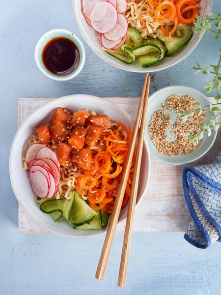 Noodles with vegetables, marinated salmon Sashimi, Carrot noodles, cucumber, radish soy sauce, sesame seeds, poke bowls, light background, copy space. Top view, overhead. Healthy clean eating concept.