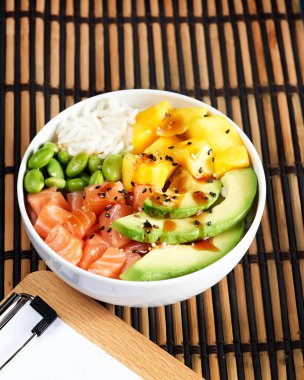 Somon balığı kasesi çiğ balık salatası Asya yemekleri, mango, soya fasulyesi edamame, pirinç, avokado, kasede servis edilmiş, mavi koyu arka plan. Kopyalama. Hızlı sağlıklı öğle yemeği, seçici odaklanma, beslenme konsepti.