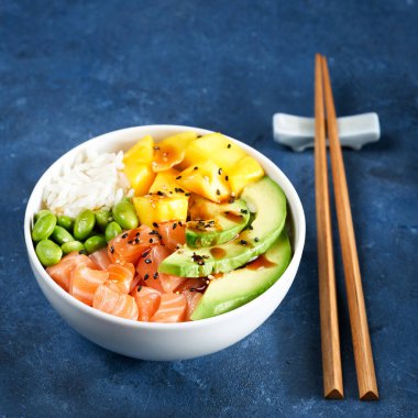 Somon balığı kasesi çiğ balık salatası Asya yemekleri, mango, soya fasulyesi edamame, pirinç, avokado, kâse, yemek çubukları, mavi arka plan. Kopya alanı, sağlıklı öğle yemeği. Seçici odak.