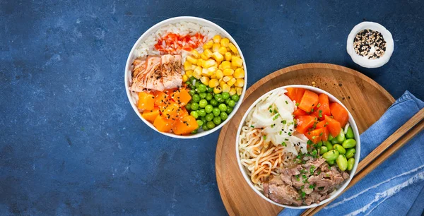 Food banner, two assorted poke bowls, flamed salmon, pulled pork, vegetables, rice, sauces. Top view, closeup. Hawaiian dish, blue dark background. Healthy and clean eating concept. Trendy asian food.