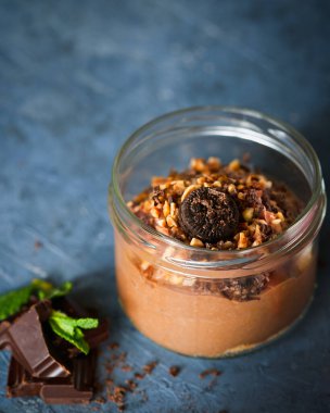 Çikolatalı kurabiyeli leziz çikolatalı mus, cam kavanozda badem ve fotokopi alanı olan koyu mavi beton arka plan. Seçici odaklanma. Yakın plan. Ev yapımı çiğ vegan çikolatalı puding..