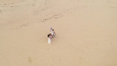Gelinler sahilde merdivende oturur ve drone etraflarında uçar. Beyaz elbiseli dört güzel kız deniz kenarındaki sahilde oturuyor.