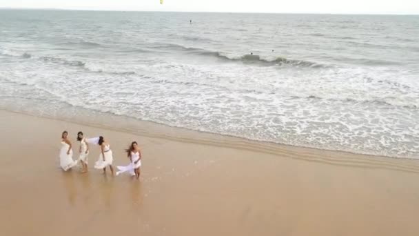 新娘们在海滩上跳舞 看到四个穿着婚纱的漂亮女孩在海边漂泊 海浪冲刷着她们的脚 与黑发女子和金发女子在海岸举行婚礼 — 图库视频影像