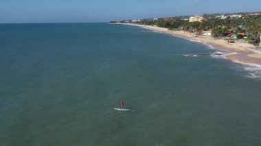 Sörf üzerinde hediye paketi olan Noel Baba. Noel Baba denizde sörf tahtasında. Adam Noel Baba kostümüyle spor yapıyor. Noel ve Yeni Yıl konsepti. Noel Baba 'ya mavi ve yeşil okyanusta kürek ve hediye çantasıyla havadan izleyeceğiz.