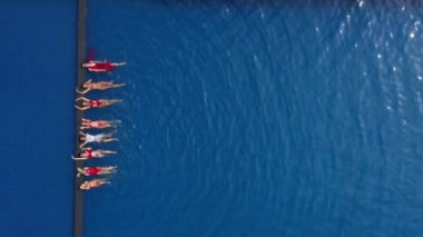 Güzel kızlar havuzda sırt üstü yatar, bacaklarını sallar, el sallar ve gülerler. Güneşli bir günde mavi suyla havuzdaki seksi kadınlara hava manzarası