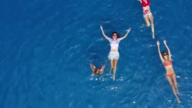 Beyaz ve kırmızı mayo giymiş seksi kızlar havuzda yüzüyor. Parlak güneşli yaz havası var. Havuz manzarası, 8 güzel kızla dolu. Kadınlar zarif bir şekilde sırt üstü yüzerler.