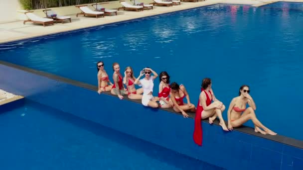プールで白と赤の水着のセクシーな愛らしい女の子の笑顔は 明るい太陽と夏の天気です 8人の美しい女の子とプールにトップの空中ビュー 彼らは座っている 楽しくキスをして — ストック動画