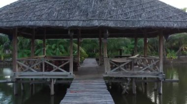 İnsansız hava aracı köprünün üzerinden havuzun ortasına doğru alçaktan uçuyor. Orada otantik bir ahşap kulübe var ve oradan uçuyor. Drone göletteki kulübeye doğru gidiyor. Gün batımı ışığı