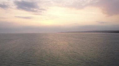 Denize ve günbatımına ait çıplak gökyüzü. Drone suyun üzerinde uçar, yumuşak günbatımı bej gökyüzü ve okyanustaki yansıması