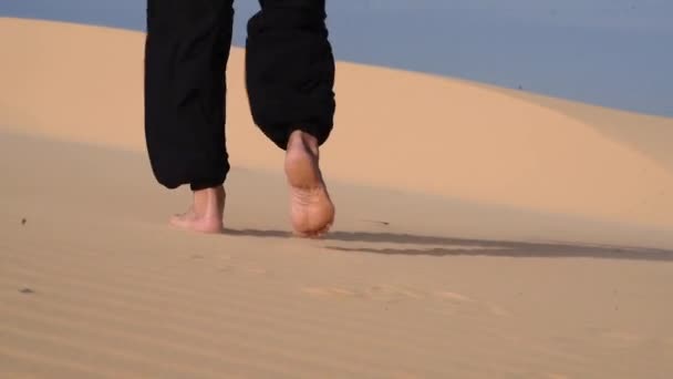 男の足のビデオを閉じると 彼は砂漠を歩いている 黒人の老人は日没時に砂丘でカンフーに従事している 砂の多くは 黄金の夕日の光 ハンサムな男の足跡 — ストック動画