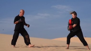 Siyah giyen yaşlı adam ve kadın gün batımında kum tepelerinde kung fu yaparlar. Bir sürü kum, altın gün batımı ışığı. Spor eğitimi. Yakışıklı erkek ve kadın kavga ediyor, tekmeler ve yumruklarla antrenman yapıyorlar.