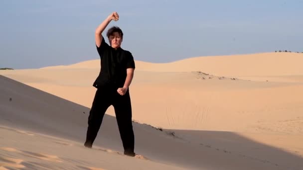 日落时 黑衣女子在沙丘上做蛇功夫 大量的沙子 金色的落日光芒 运动训练 一个漂亮的成年女子在沉思 沙漠培训 — 图库视频影像