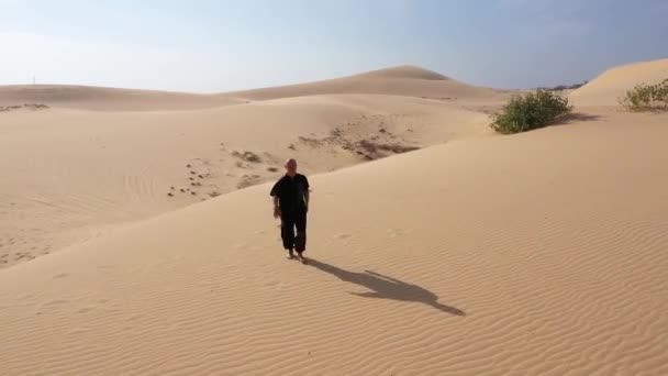 日落时 身穿黑色衣服的老人在沙丘上练习功夫 大量的沙子 金色的落日光芒 运动训练 英俊的男人在沉思 男子走向相机 带背景光的鸟瞰 — 图库视频影像