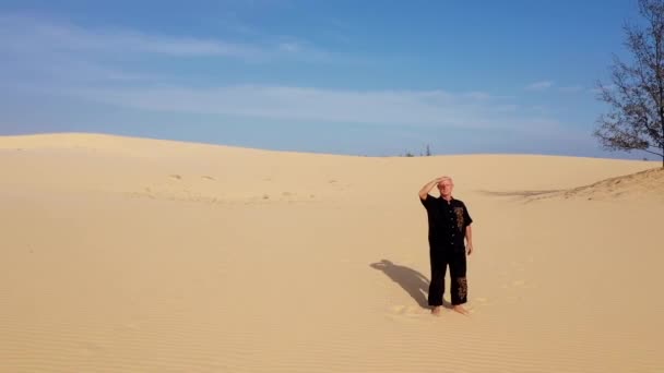 日落时 身穿黑色衣服的老人在沙丘上练习功夫 大量的沙子 金色的落日光芒 运动训练 英俊的男人在沉思 空中观察沙漠与黑衣人一起训练 — 图库视频影像