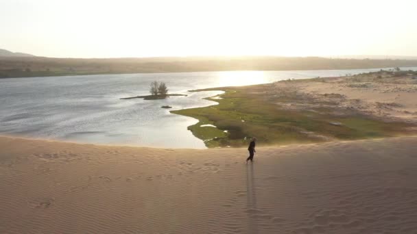 湖と砂漠への空中ビュー 黒人の老人は日没時に砂丘でカンフーに従事している 砂の多くは 黄金の夕日の光 スポーツトレーニング ハンサムな男が歩いている 美しい風景 — ストック動画
