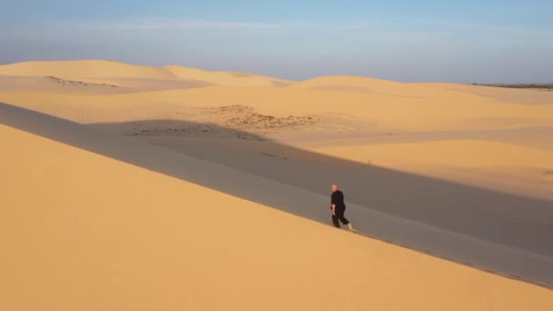 人在沙漠中越飞越高 日落时 身穿黑色衣服的老人在沙丘上练习功夫 大量的沙子 金色的落日光芒 运动训练 英俊的男人沉思着 — 图库视频影像