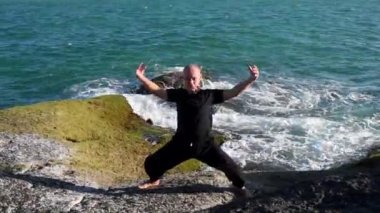 Kung fu ustası kayalıklarda pratik yapıyor, kamera siyah giyen yaşlı bir adamın eğitimini gösteriyor, sonra kayalarda kırılan bir dalgaya dönüyor, denizin spreyine.
