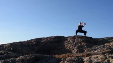 Siyah giyen bir adam dağda durur. Savaşçı pozu, meditasyon, yoga, spor, kung fu. Mavi gökyüzü