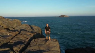 Siyahlı kadın denizin kenarındaki bir uçurumun kenarında duruyor, bir dron üzerinden uçuyor, gökyüzünü, mavi denizi ve gemiyi görebilirsiniz.