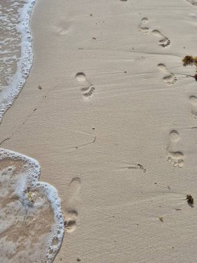 Okyanus köpüğünün yanındaki kumlu sahilde insan ayak izleri.