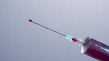 Kırmızı damlalar beyaz arka planı olan bir şırıngadan gelir.