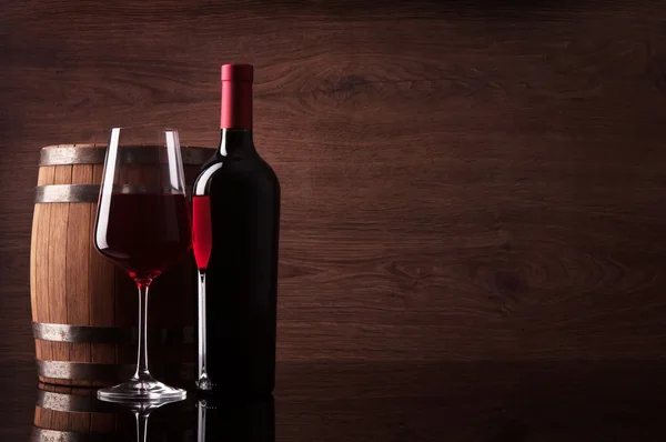 Bottle of red wine, glass and barrel on dark wooden background — Stock Photo, Image