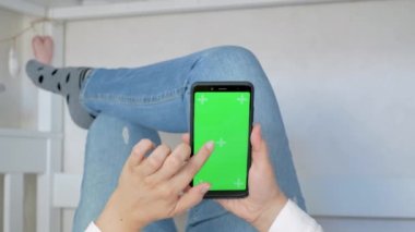 Yeşil ekran ve krom anahtarı olan bir telefon. Rahatlama konsepti. Green Mock-up Screen ile Smartphone kullanarak Kanepede uzanan, Swiping, Scrolling Jestleri yapan kadın. Cep Telefonu Kullanan Kız